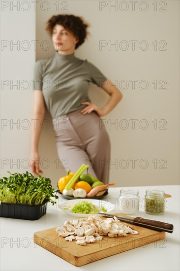 Kitchen table with fresh organic vegetables and blurred young woman on background leaning against