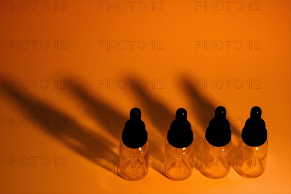 Four glass eye dropper bottles with dark black shadows on golden orange background. A little noise