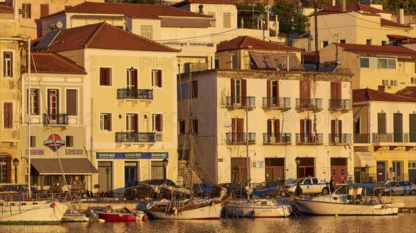 The last rays of sunshine of the day cosily illuminate the waterfront with cafes and boats, Gythio,