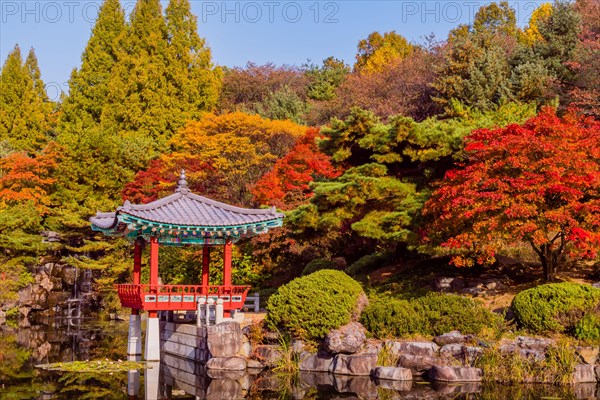 Beautiful oriental gazebo with terracotta tile roof at edge of man made pond with small waterfall