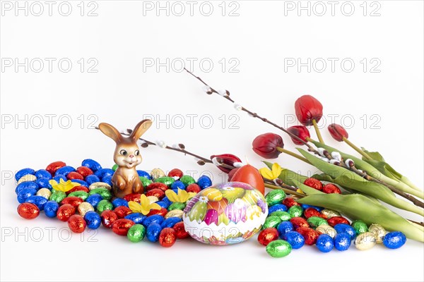 A collection of colourful chocolate eggs and an Easter bunny next to tulips and palm catkins, white