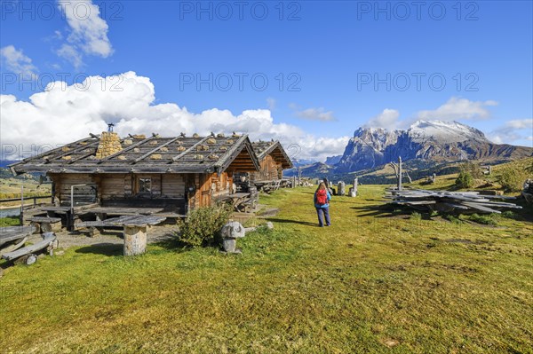 Edelweiss hut on Alpe di Siusi, hiker with red rucksack, Sassopiatto and Sassolungo, clouds,