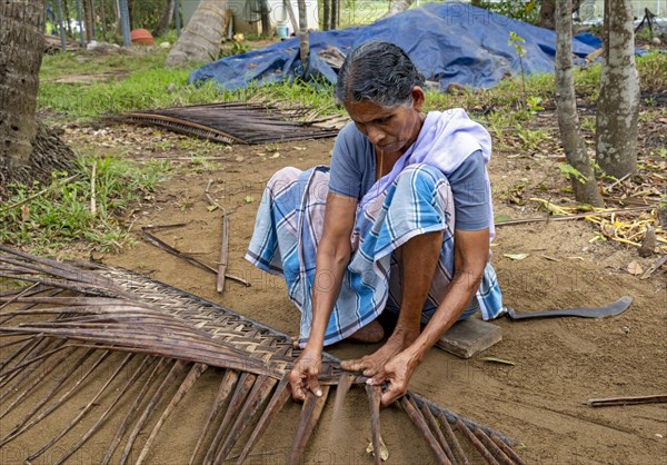 A village woman demonstrates the traditional craft of making mats from coconut leaves using her