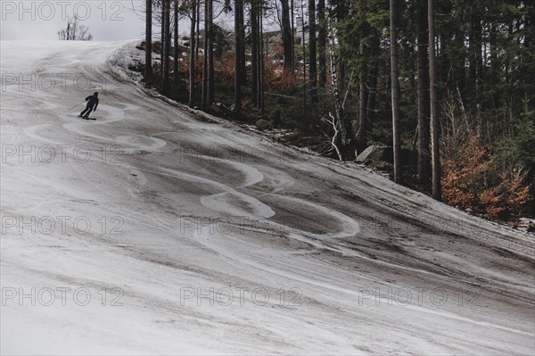 A skier skis on an artificially snow-covered and dirty slope, taken on a ski slope in the Jizera