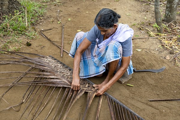 A village woman demonstrates the traditional craft of making mats from coconut leaves using her