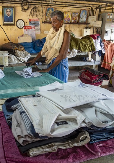 A man irons shirts with an antique iron at Dhobi Khana Public Laundry, Fort Kochi, Cochin, Kerala,