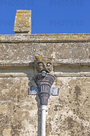Gargoyle grotesque face drainpipe on wall medieval church of Saint John, Inglesham, Wiltshire,
