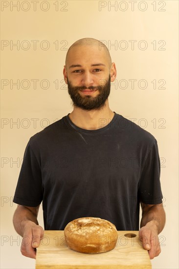 Head and shoulder portrait Caucasian white young man shaven head and beard holding fresh loaf of