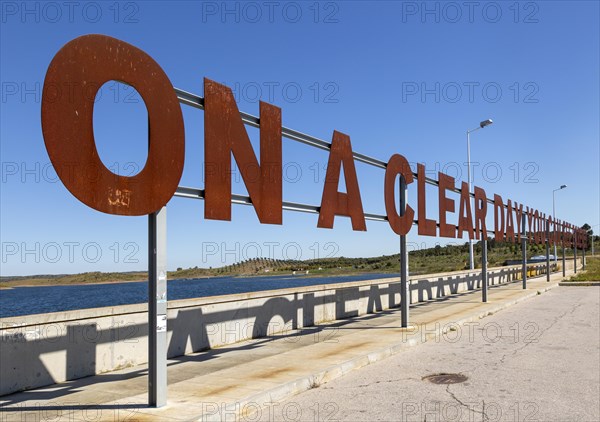 Large red rusty capital letters ON A CLEAR DAY YOU CAN SEE FOREVER blue sky background, Alqueva