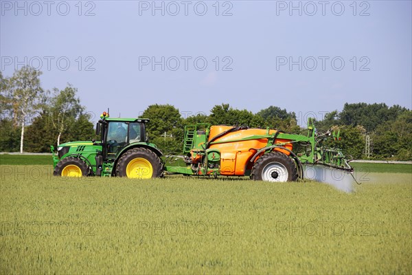 A farmer drives his tractor with a crop protection sprayer across his wheat field to combat brown