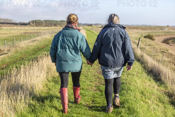 Mother and adult daughter walking together by the River Ore, Suffolk, England, UK from behind