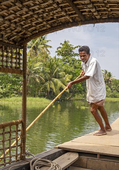A man navigates a boat through the canals of the Kerala Backwaters using a long pole, Vembanad
