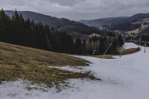 A melting ski slope next to a meadow, taken on a ski slope in the Jizera Mountains ski area near