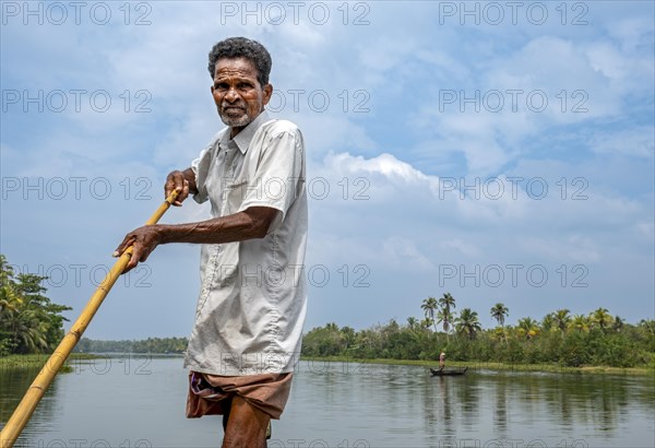 A man navigates a boat through the canals of the Kerala Backwaters using a long pole, Vembanad
