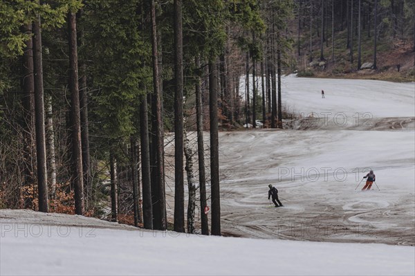 Skiers skiing on an artificially snow-covered and dirty slope, taken on a ski slope in the Jizera
