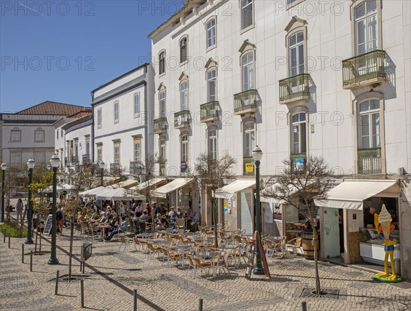 People sitting in sunshine outside street cafes in Praca da Republica, Tavira, Algarve, Portugal,