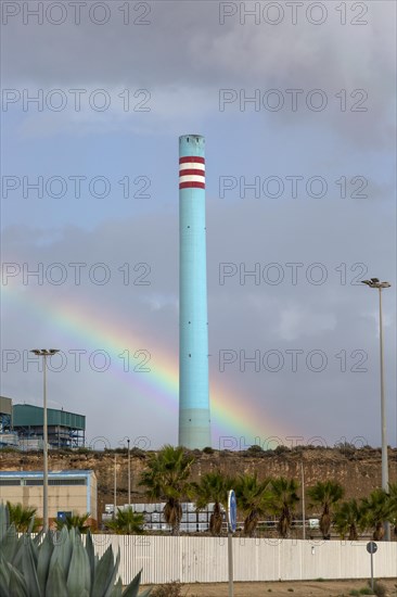 Rainbow in stormy sky behind tall blue industrial cement factory chimney, Carboneras, Almeria,