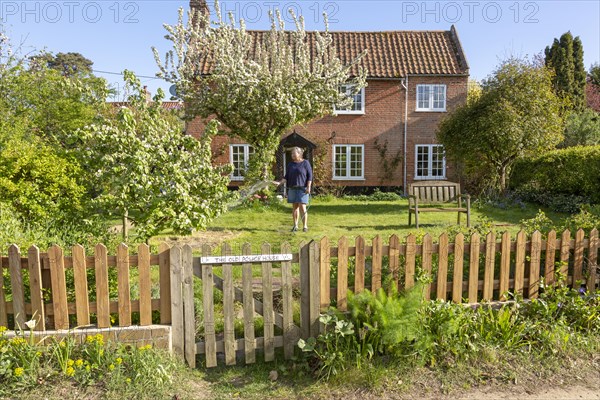 Woman watering garden with hosepipe in front of red brick historic detached house, Shottisham,