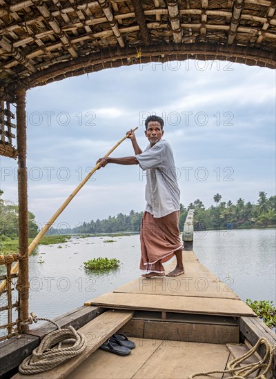 A man navigates a boat through the canals of the Kerala Backwaters using a long pole, Vembanad