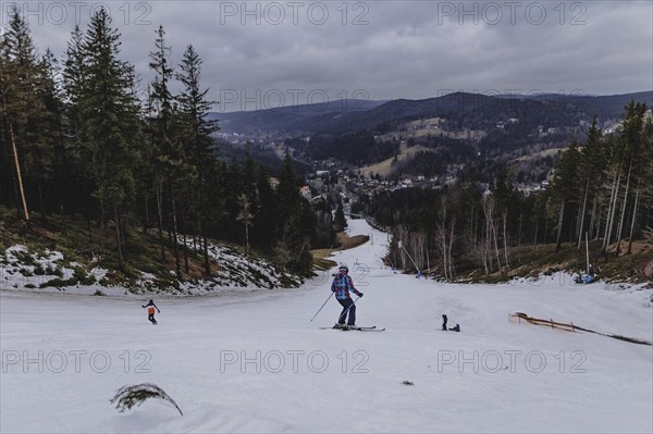 Skiers skiing on an artificially snow-covered and dirty slope, taken on a ski slope in the Jizera