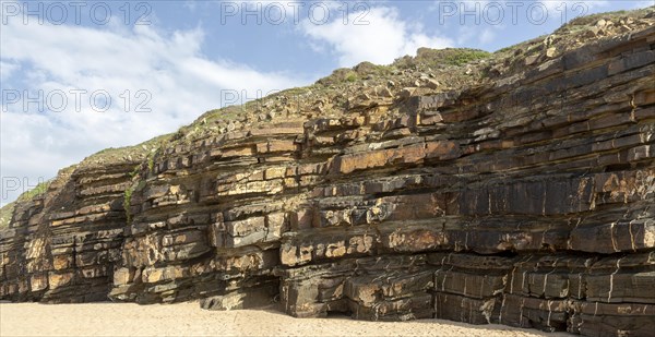 Tilted layers showing bedding planes in strata of sedimentary rock in coastal cliff at Odeceixe,
