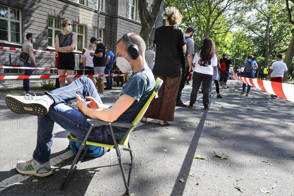 A vaccinated person sits on his folding chair in a long queue. Neighbourhood residents in the