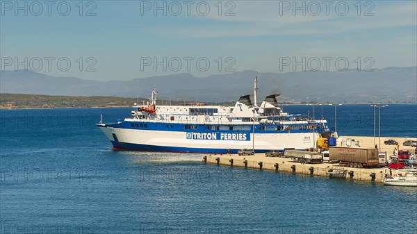 Ferry in the harbour loaded with trucks, surrounded by sea and mountains under a blue sky, Gythio,