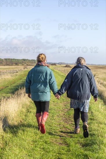Mother and adult daughter walking together by the River Ore, Suffolk, England, UK from behind