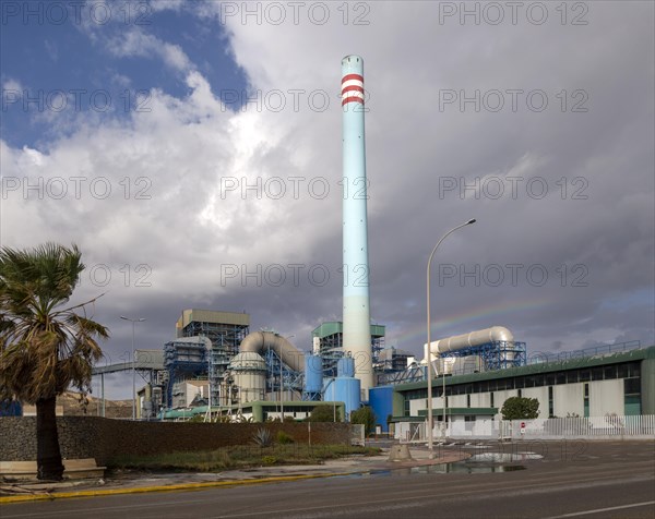 Rainbow in stormy sky behind tall blue industrial cement factory chimney, Carboneras, Almeria,