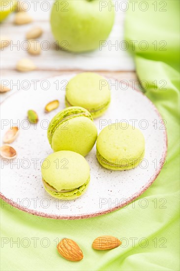 Green macarons or macaroons cakes with cup of coffee on a white wooden background and green linen