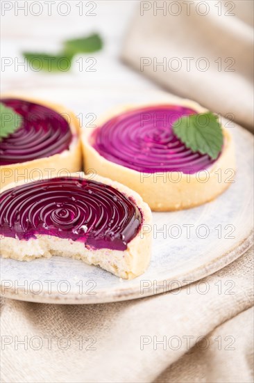 Sweet tartlets with jelly and milk cream with cup of coffee on a white wooden background and linen