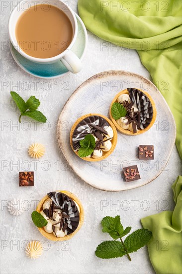 Sweet tartlets with chocolate and cheese cream with cup of coffee on a gray concrete background and