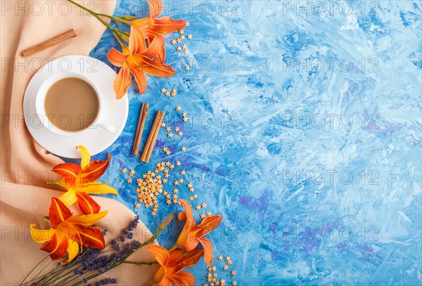 Orange day-lily and lavender flowers and a cup of coffee on a blue concrete background, with orange