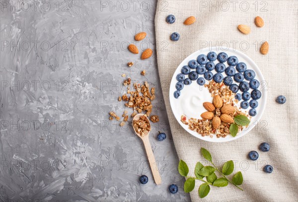 Yoghurt with blueberry, granola and almond in white plate with wooden spoon on gray concrete