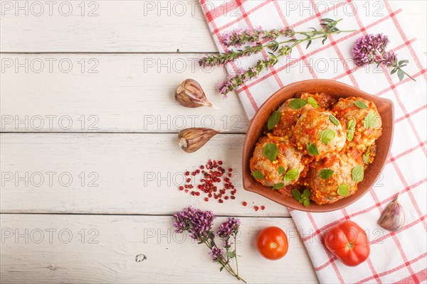 Pork meatballs with tomato sauce, oregano leaves, spices and herbs in clay bowl on a white wooden