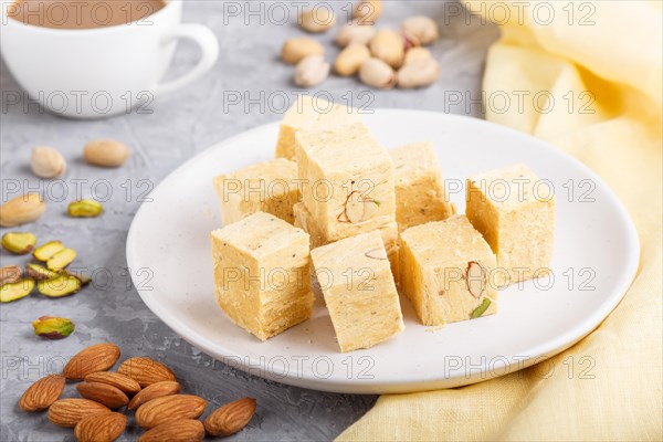 Traditional indian candy soan papdi in white plate with almond, pistache and a cup of coffee on a