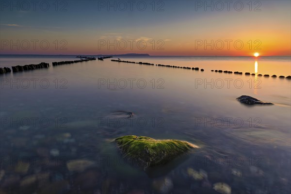 Sunset at the double stage in Dranske on the island of Ruegen. A green stone overgrown with algae