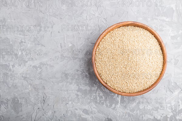 Wooden bowl with raw white quinoa seeds on a gray concrete background. Top view, flat lay, copy