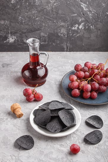 Black potato chips with charcoal, balsamic vinegar in glass, red grapes on a blue ceramic plate on