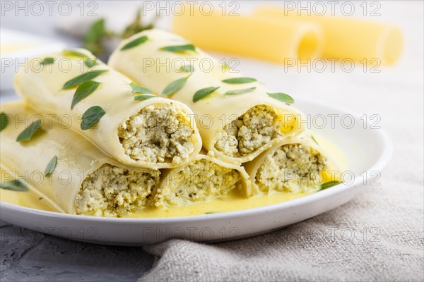 Cannelloni pasta with egg sauce, cream cheese and oregano leaves on a gray concrete background with
