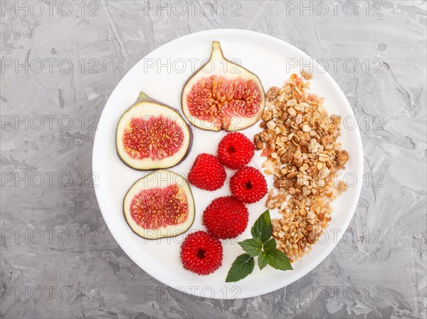 Yoghurt with raspberry, granola and figs in white plate on a gray concrete background top view,