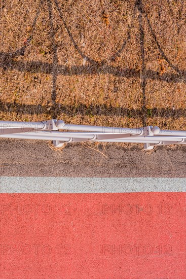 Looking down onto red bike path next to metal guardrail casting its shadow on brown grassy area in