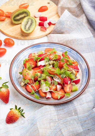 Vegetarian fruits and vegetables salad of strawberry, kiwi, tomatoes, microgreen sprouts on white