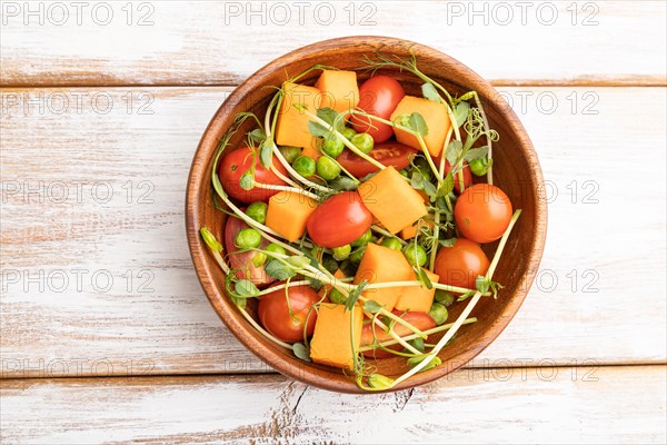 Vegetarian vegetable salad of tomatoes, pumpkin, microgreen pea sprouts on white wooden background.