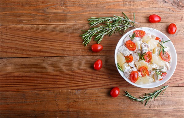 Chicken fillet salad with rosemary, pineapple and cherry tomatoes on brown wooden background. top