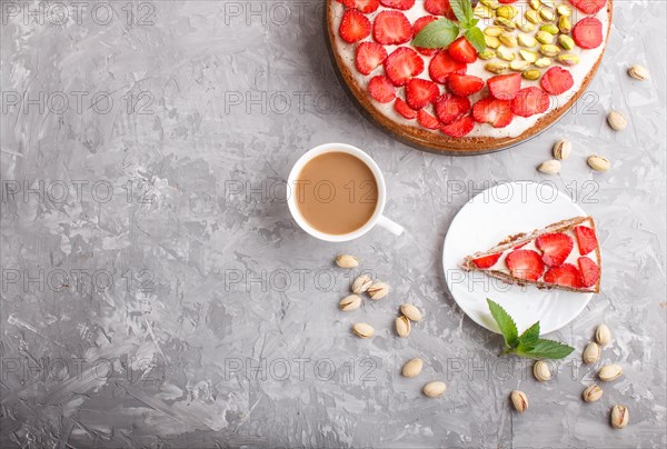 Homemade cake with yoghurt cream, strawberry, pistachio and a cup of coffee on a gray concrete