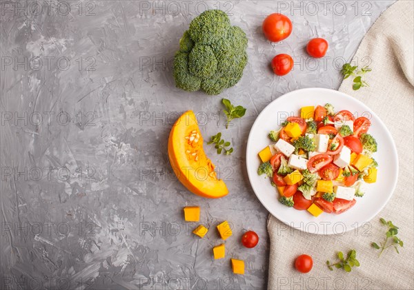 Vegetarian salad with broccoli, tomatoes, feta cheese, and pumpkin on white ceramic plate on a gray