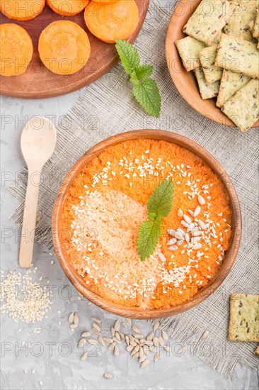 Carrot cream soup with sesame seeds and snacks in wooden bowl on a gray concrete background with