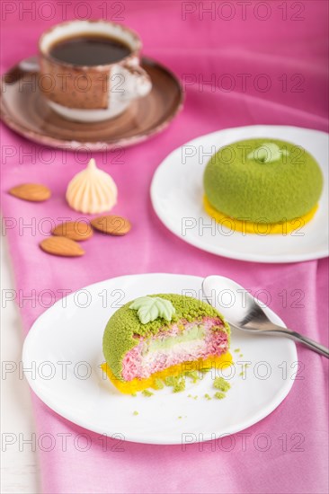 Green mousse cake with pistachio and strawberry cream on a white wooden background and pink textile