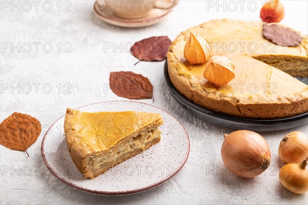 Autumn onion pie decorated with leaves and cup of coffee on gray concrete background. Side view,